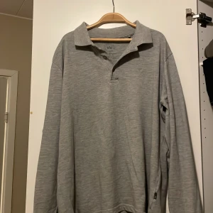 Grå pikétröja från Kronstadt - Säljer en stilren grå pikétröja från Kronstadt i bra skick. Den har långa ärmar och en klassisk krage med knappar. Perfekt för både vardag och lite mer uppklädda tillfällen. Skön och enkel att matcha med det mesta i garderoben. Använd vid ett få tillfällen så gott som ny! 