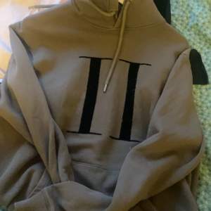 Säljer en snygg beige hoodie från Les Deux med en stor svart romersk tvåa på framsidan. Den har en klassisk känguruficka och justerbar dragsko i huvan. Perfekt för en avslappnad stil eller en chill dag hemma. Passar till det mesta och är superbekväm!