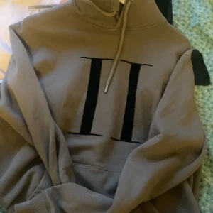  hoodie från Les Deux - Säljer en snygg beige hoodie från Les Deux med en stor svart romersk tvåa på framsidan. Den har en klassisk känguruficka och justerbar dragsko i huvan. Perfekt för en avslappnad stil eller en chill dag hemma. Passar till det mesta och är superbekväm!