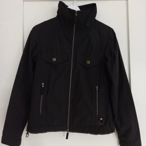 Svart vindjacka från Luhta - Säljer en elegant svart vindjacka från Luhta i fint skick. En dragkedja framtill och praktiska fickor med dragkedjor. Perfekt för höst och vinter med sin stilrena design och funktionella detaljer. Tecken på användning: saknas en tyg detalj på ena jackfickan (se bild 4)💕