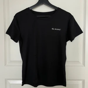 Svart t-shirt från SOC - Snygg och enkel svart t-shirt från SOC i syntetmaterial. Perfekt för träning eller vardagsbruk. Den har en normal passform och korta ärmar, med SOC-loggan tryckt på bröstet. Ett måste i garderoben för en stilren look!