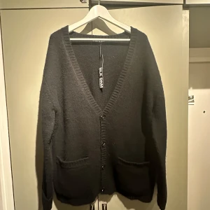 Svart kofta från BLK DNM - Säljer en stilren svart kofta från BLK DNM i storlek M (herr) passar dam storlek 40-44. Den är gjord av 100% ull och har en djup v-ringning med knappar framtill. Perfekt för både höst och vinter, och den har praktiska fickor. Supermysig och varm!