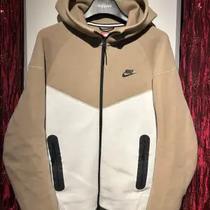 Säljer en snygg och bekväm hoodie från Nike i beige och vit. Den har en dragkedja framtill och en klassisk Nike-logga på bröstet. Perfekt för höst och vår, med långa ärmar och en skön huva. Passar både till träning och vardag. hör av er vid minsta fundering 🍾