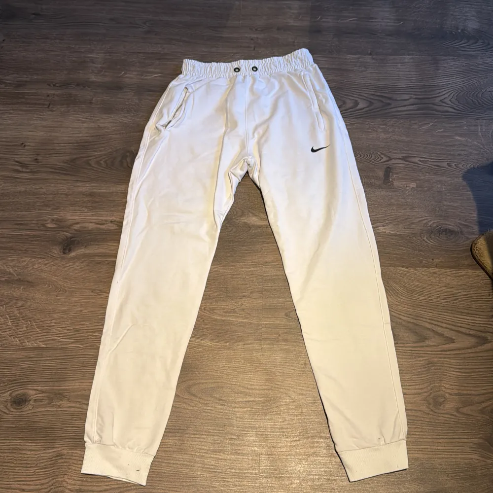 Säljer ett par vita mjukisbyxor från Nike i bra skick. De har en elastisk midja med snörning och muddar vid bensluten. Perfekta för en avslappnad stil eller träning. Byxorna har också fickor och den klassiska Nike-loggan på ena benet.. Jeans & Byxor.