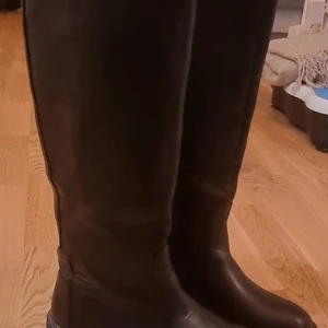Svarta höga stövlar - Säljer ett par svarta höga stövlar med grov sula. Perfekta för höst och vinter med sin robusta design. De har en dragkedja på sidan för enkel på- och avtagning. Passar både till vardags och lite tuffare väder.