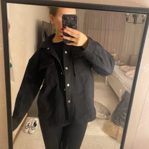 Svart jacka med knappar - Säljer en svart jacka i mycket bra skick. Den har en normal passform och är perfekt för höst och vår. Jackan har långa ärmar och stängs med knappar framtill. Den är stilren och enkel att matcha med olika outfits.