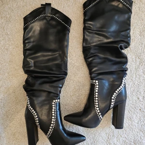 Svarta stövlar med nitar från RAID - Snygga svarta stövlar från RAID med coola nitar längs kanterna. De har en hög klack och spetsig tå, vilket ger en elegant look. Perfekta för höst och vinter, och funkar lika bra till fest som till vardags. Stövlarna är i mycket bra skick och redo för nya äventyr!