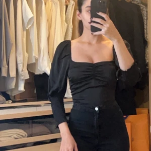 Svart offshoulder topp - Snygg svart offshoulder topp med puffiga ärmar och rynkdetaljer framtill. Perfekt för en utekväll eller fest. Toppen har en tight passform som framhäver figuren.