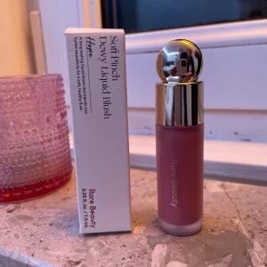 Soft Pinch Dewy Liquid Blush från Rare Beauty - Säljer en Soft Pinch Dewy Liquid Blush i nyansen 'Hope' från Rare Beauty. Denna flytande rouge kommer i en elegant flaska med en rundad silverfärgad kork. Perfekt för att ge kinderna en naturlig och fräsch glöd. Använd endast en gång, på handen!💗