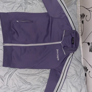 Lila track jacket från Palm Angels M/L - Snygg lila track jacket från Palm Angels med vit dragkedja och vita ränder längs ärmarna. Passar för storlek M och L