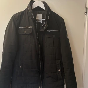 Svart jacka från J.Lindeberg - Snygg svart jacka från J.Lindeberg med dragkedja och knappar. Jackan är nyskick. Perfekt för höst och vår.