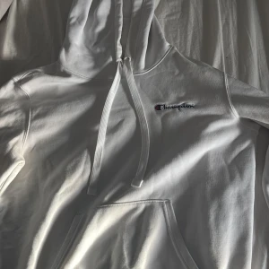 Vit hoodie från Champion - Säljer en klassisk vit hoodie från Champion med broderad logga på bröstet. Den har en stor ficka framtill och justerbar huva med dragsko. Den har en pytteliten fläck på vänster ärm (se bild 4) men inget man tänker på. Storlek S 