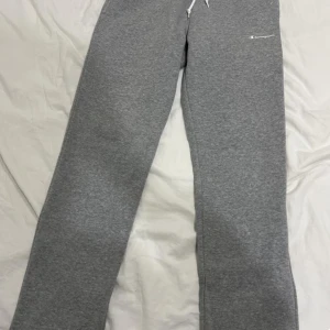 Grå mjukisbyxor från Champion - Säljer ett par grå mjukisbyxor från Champion med snörning i midjan. Perfekta för en avslappnad stil och bekväma att bära. Byxorna har en normal passform och är tillverkade i mjukt material. STORLEK: S