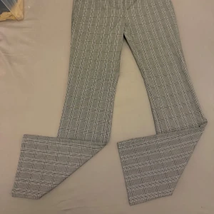 Rutig byxa från NA-KD - Snygga gråa rutiga byxor från NA-KD. De har en klassisk design med lite utsvängda ben och hög midja, perfekt för en stilren look. Byxorna är tillverkade i ett bekvämt material som passar både till vardags och mer uppklädda tillfällen.