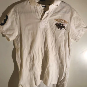 Vit kortärmad pikétröja från Ralph Lauren - Säljer en klassisk vit pikétröja från Ralph Lauren med broderad logga på bröstet. Tröjan har korta ärmar och knappar vid kragen. Perfekt för en stilren och avslappnad look.