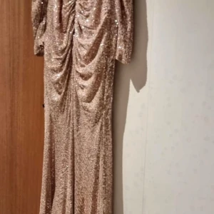 Glittrig långklänning i champagne - Använt en gång från REMANNS BRÖLLOPSBUTIK, köpt för 3400kr. Det är en elegant långklänning i champagnefärg med glittrande paljetter. Klänningen har långa ärmar och en smickrande drapering på baksidan. Perfekt för en glamorös kväll. OBS PRIS KAN DISKUTERAS!