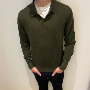 Olivgrön pikétröja - Snygg olivgrön pikétröja med krage och knappar framtill. Perfekt för en stilren och avslappnad look. Tröjan har långa ärmar och en klassisk passform.