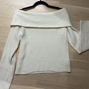 Vit offshoulder stickad tröja - Säljer en stilren vit offshoulder tröja i stickat material. Tröjan har långa ärmar och en ribbad design som ger en snygg och bekväm passform. Knappt använd! Passar både storlek S och M