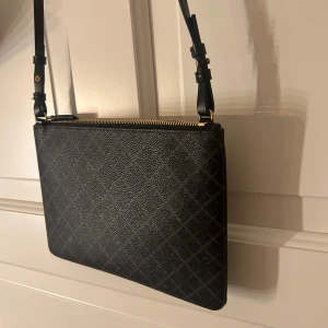 Malene birger väska - Snygg svart axelväska med ett subtilt rutigt mönster. Väskan har en justerbar axelrem. Org pris= 899kr