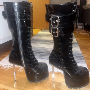 Svarta platåstövlar med korsklack - Dollskill - Snygga svarta platåstövlar i lack med unika korsformade klackar. Stövlarna har dragkedja samt snörning om man vill ha smalare eller större vid smalbenen så passar många! Köpte på Dollskill typ 2 år sen men har nog bara använt 2-3 ggr max. Är lite dammiga men polerar självklart upp dem innan frakt!