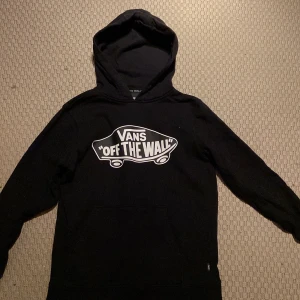 Svart hoodie från Vans - Säljer en svart hoodie från Vans med det klassiska 'Off The Wall' trycket på framsidan. Tröjan har en stor huva och långa ärmar, perfekt för en avslappnad stil och dem som gillar skate förstås. Säljer den då den är för liten, pris kan diskuteras.