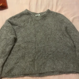 Grå ulltröja från Soft Goat  - Mysig grå tröja från Soft Goat i ull. Perfekt för kyliga dagar med sin fluffiga och mjuka textur. Tröjan har en enkel design med långa ärmar och rund halsringning.