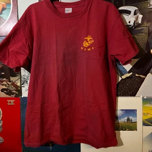 Single stitch Röd USMC t-shirt från T-Shirt Factory - Säljer en röd t-shirt från T-Shirt Factory med USMC-tryck på bröstet och MARINES-tryck på ryggen. Finns tyvärr ett hål på framsidan som man ser på bild 2. Annars mycket bra cond