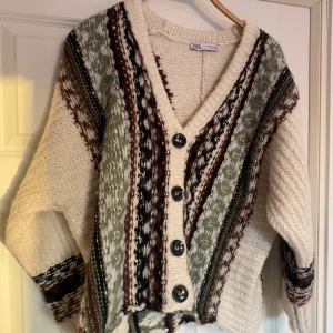 Mönstrad kofta från Zara - Säljer en mysig kofta från Zara i cremevit med mönster i brunt och grönt. Koftan har en v-ringad design med stora knappar framtill och långa ärmar. Perfekt för kyliga dagar! Aldrig använd, endast provad.