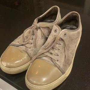  Lanvin bruna  - Snygga bruna sneakers från Lanvin i mocka med snörning och gummisula. Perfekta för en avslappnad stil. Tar bara swisha.