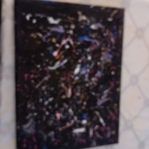 Abstrakt konstverk i mörka färger - Säljer ett abstrakt konstverk med en mörk bakgrund och färgstänk i rosa, blått, vitt och gult. Tavlan har en rektangulär form och är inramad i svart. Perfekt för att ge rummet en modern och konstnärlig touch.