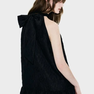 Svart klänning med rosett - Elegant svart ärmlös klänning med en fin rosett i ryggen. Klänningen har en lös passform och en volangdetalj vid fållen. Perfekt för en stilren look. Endast testad❤️❤️