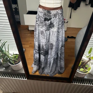 Mönstrad långkjol i grå toner - Säljer en långkjol med ett unikt mönster i olika grå nyanser. Kjolen har en luftig passform och är perfekt för en avslappnad stil. Den är tillverkad i ett mjukt och bekvämt material.