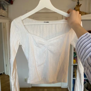 Vit långärmad topp med rynkdetalj - Säljer en söt vit långärmad topp med rynkdetalj framtill. Toppen har ett diskret randigt mönster och en v-ringad design🤗 använts mycket men den är i jättebra skick💕
