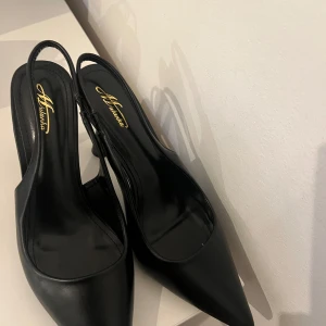 Svarta pumps med klack - Eleganta svarta pumps från Alaïa med spetsig tå och stilren design. Skorna har en smal rem runt hälen och en unik klackform som ger en modern touch.