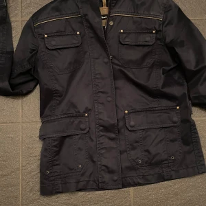 Svart jacka med dragkedja och knappar - Snygg svart jacka med dragkedja och knappar. Den har flera praktiska fickor och en stilren design. Perfekt för höst och vår.