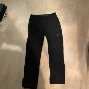 Svarta byxor från Haglöfs - Snygga svarta byxor från Haglöfs, perfekta för utomhusaktiviteter. De har en rak passform och praktiska fickor. Byxorna är tillverkade i ett slitstarkt material som passar bra för vandring och andra äventyr. Helt nya fick dom i julklapp men har ingen användning för dom 