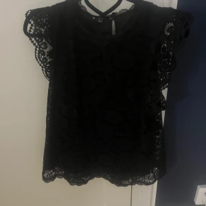 Svart spetsblus - Elegant svart blus med spetsdetaljer och korta ärmar. Perfekt för en stilren look med vackra mönster och en feminin touch.