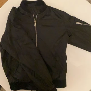 Svart bomberjacka från Peak Performance - Snygg svart bomberjacka från Peak Performance med dragkedja framtill och en ficka med dragkedja på ärmen. Perfekt för en stilren look. Jackan är självklart äkta och är i ett mycket bra och fräscht skick! 