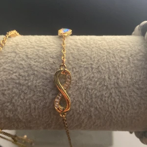 Guldarmband med oändlighetssymbol - Elegant guldarmband med en oändlighetssymbol dekorerad med små glittrande stenar. Perfekt för att lägga till en touch av stil och elegans till din look.