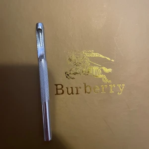 Burberry bälte med monogramspänne - Säljer ett stilrent Burberry bälte med ett stort blått monogramspänne. Bältet har det klassiska Burberry-mönstret i beige, rött och svart. Perfekt för att ge en lyxig touch till din outfit. Kommer med originalpåse och förpackning. Allt ingår kvitto,påsen, boxen osv 