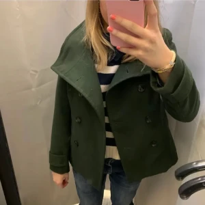 Grön kappa - Snygg grön kappa med dubbelknäppning och bred krage. Perfekt för kyligare dagar och ger en stilren look. Passar bra till både jeans och mer uppklädda outfits.