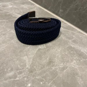 Blått flätat grisch bälte - Snyggt blått flätat bälte med silverfärgat spänne. Perfekt för att ge en stilren touch till din outfit. Bältet har en klassisk design och är lätt att matcha med olika kläder. 100cm