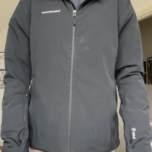 Svart jacka från Peak Performance - Snygg svart skidjacka från Peak Performance med dragkedja och huva. Perfekt för kyligare dagar med sin stilrena design och praktiska fickor.