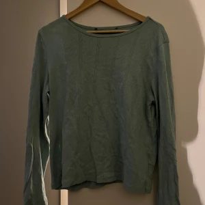 Grön långärmad tröja med mönster - Säljer en stilren grön långärmad tröja med diskret mönster från Lager157. Perfekt för en avslappnad look. Tröjan har en rund halsringning och är tunn. Lappen är avklippt men annars som ny.