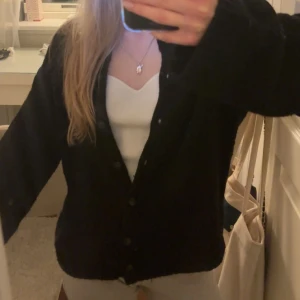 Svart kofta med knappar - Mysig svart kofta med knappar framtill. Perfekt för kyliga dagar och enkel att matcha med olika outfits.  Den är använd en del men har inga skador!