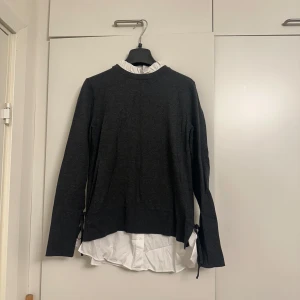 Svart långärmad tröja med vit krage - Elegant svart långärmad tröja med vit krage och nederdel som ger en lager-på-lager-look. Perfekt för en stilren och klassisk outfit.