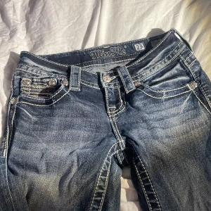 Blå jeans från Miss Me - Snygga blå jeans från Miss Me med coola detaljer och slitningar. De har en låg midja och en straight passform. Perfekta för en avslappnad stil med en touch av bling på bakfickorna.
