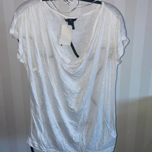 Vit topp från H&M - Säljer en vit topp från H&M , ny med korta ärmar och en avslappnad passform. Toppen har en djup v-ringning och är tillverkad i ett lätt och luftigt material, perfekt för varmare dagar.