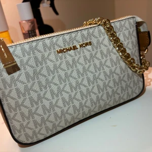 Beige kuvertväska från Michael Kors - Köpt för 1689kr. Snygg beige kuvertväska från Michael Kors. Väskan är perfekt för att bära det viktigaste. Den eleganta designen gör den till ett stilrent val för olika tillfällen. Ändast gått ut med denna 3 gånger.