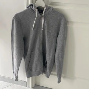 Tröja  - En grå tjocktröja med luva och dragkedja. 